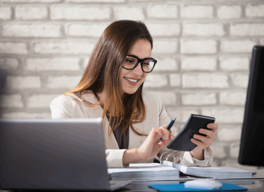 ChatGPT said: A smiling accountant reviews documents and works on a calculator at her desk, representing financial review and compliance for a nonprofit single audit.