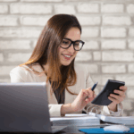 ChatGPT said: A smiling accountant reviews documents and works on a calculator at her desk, representing financial review and compliance for a nonprofit single audit.