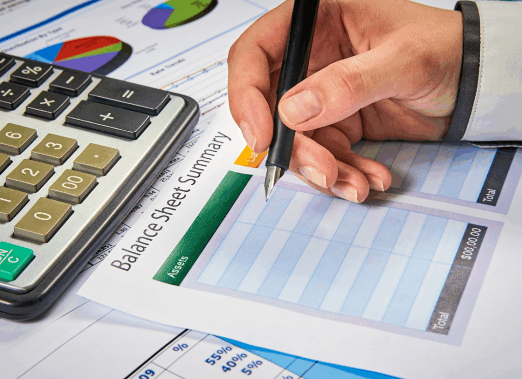 A person reviews financial documents with a calculator and a balance sheet summary, illustrating how to prepare a construction company balance sheet.