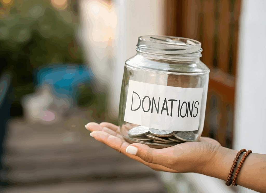 A person holds a clear glass jar labeled “Donations,” partially filled with coins, symbolizing charitable giving and community support.