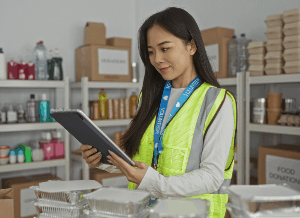 A volunteer in a safety vest reviews information on a tablet in a donation center to prepare for a single audit at a nonprofit organization.