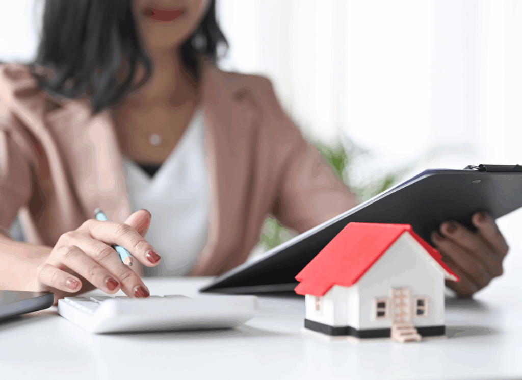 Real estate professional reviews financial projections on a tablet and calculator beside a model home, illustrating a real estate pro forma analysis.