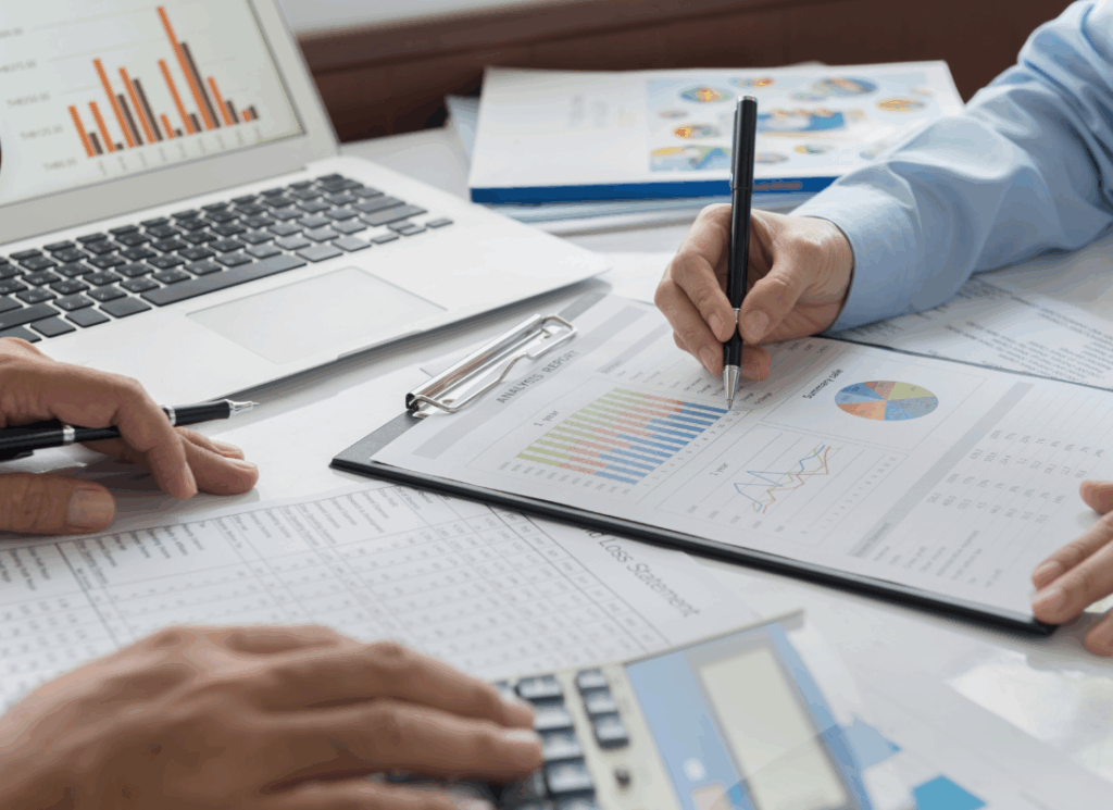 Two dental accounting professionals review financial charts and reports with a laptop and calculator on the table, illustrating detailed analysis for Dental Business Consulting.