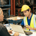 A manufacturing worker reviews costs on a tablet with a manager, illustrating job costing for manufacturing during a production planning discussion.