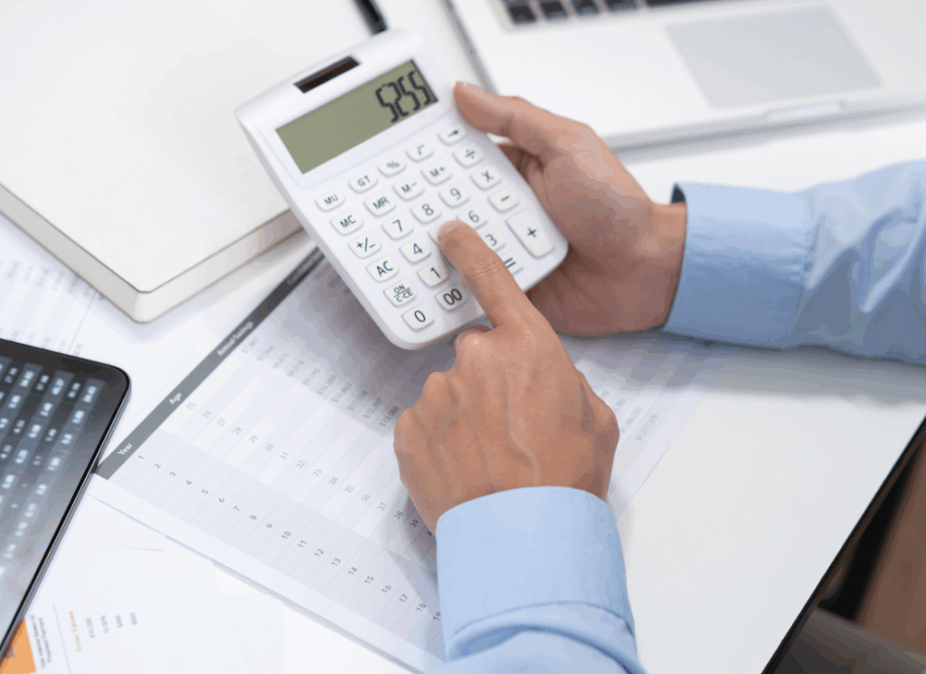 A CPA using a calculator over financial spreadsheets at a desk, reviewing figures related to a manufacturing chart of accounts.