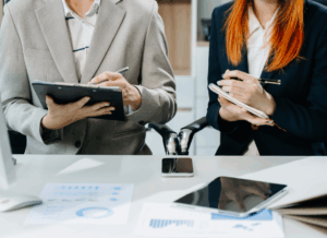 Two nonprofit professionals review reports and take notes at a desk, analyzing data and charts for Nonprofit Financial Statements.