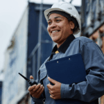 Woman working at construction site wearing hardhat and carrying clipboard