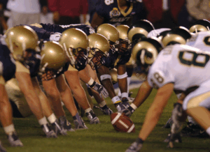 Two football teams lined up with the ball between them as they're about to start play.