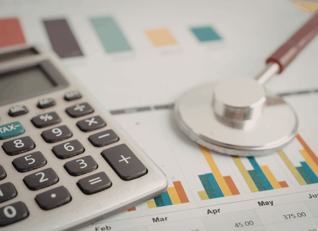 A calculator and stethoscope rest on financial charts, illustrating rcm in medical billing and the analysis of healthcare revenue performance.