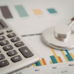 A calculator and stethoscope rest on financial charts, illustrating rcm in medical billing and the analysis of healthcare revenue performance.