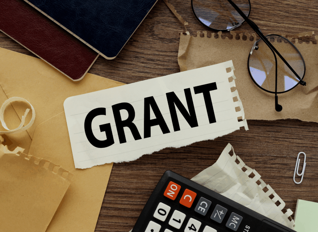Desk with calculator, notebooks, and a paper labeled “Grant,” representing grant management best practices and organized financial oversight.