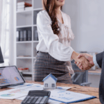Two real estate professionals shake hands over financial reports and a model house, illustrating how are partnerships taxed in real estate and business deals.