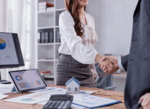 Two real estate professionals shake hands over financial reports and a model house, illustrating how are partnerships taxed in real estate and business deals.