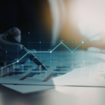 someone holding a pen to financial analysis charts, with an overlay of computerized financial charts