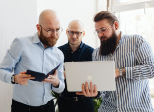 three office workers with concerned expressions as they look at something on a laptop screen