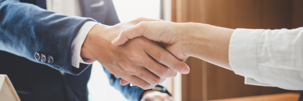 Close-up of a handshake between a person in a navy blazer and a person in a white shirt.