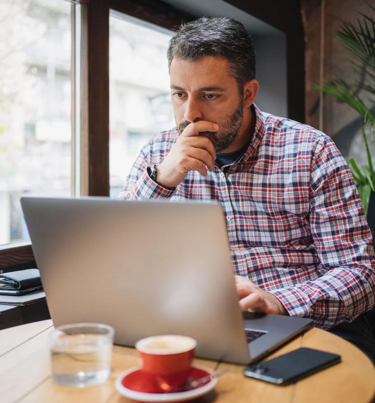 Contemplative manager sitting at a small table viewing something on his laptop