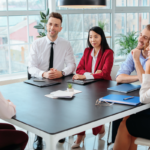 Hiring team interviewing a candidate at a conference table in a bright office setting.
