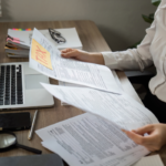 Person reviewing tax documents at a desk with a laptop and paperwork, analyzing forms for advanced retirement planning strategies.