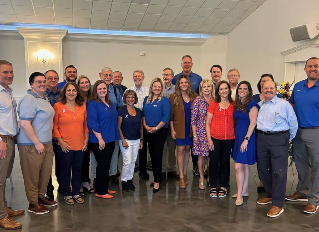 Group photo of the James Moore team standing together indoors, smiling and dressed in business casual attire during a team gathering.