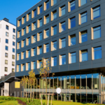 Modern multi-story commercial building with large windows and contemporary architectural design in an urban development area.