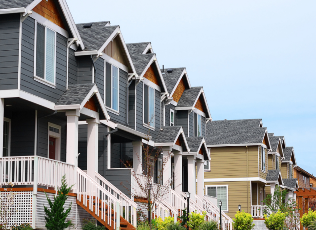 Row of modern suburban townhomes with gray and beige siding, front porches, and staircases in a residential neighborhood.