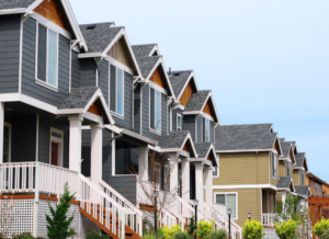 Row of modern suburban townhomes with gray and beige siding, front porches, and staircases in a residential neighborhood.