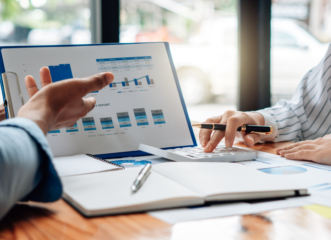 Two nonprofit professionals review financial charts and graphs on a report while using a calculator during a business meeting.