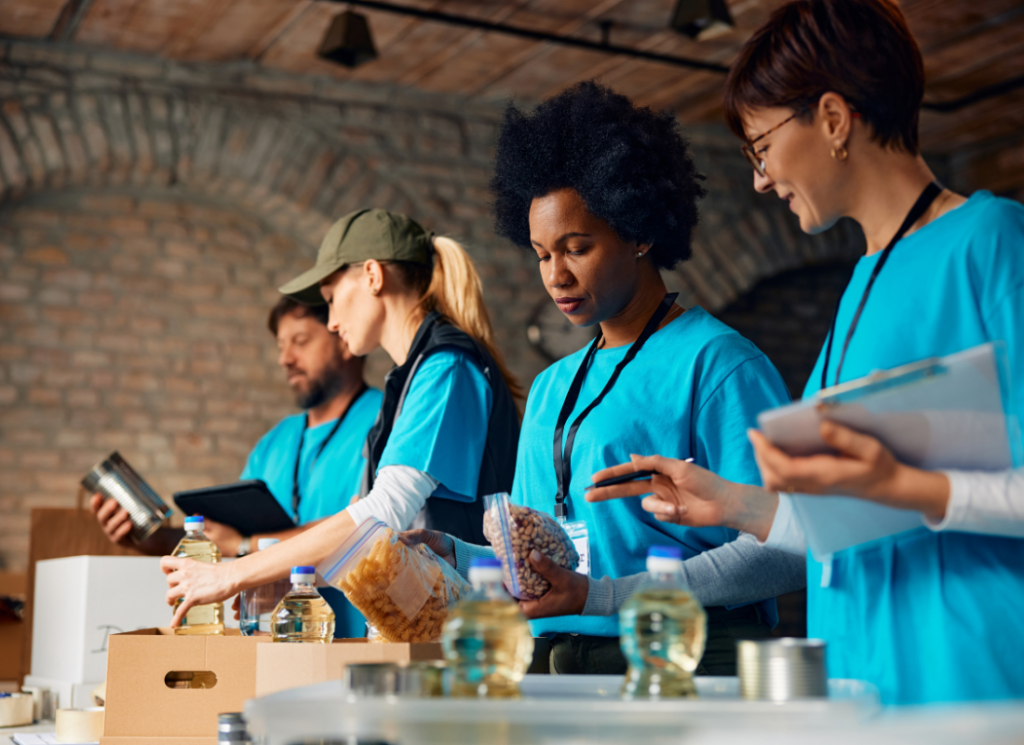 Volunteers at a nonprofit wearing matching shirts sort and pack food donations, including canned goods and pantry items, at a community distribution site.