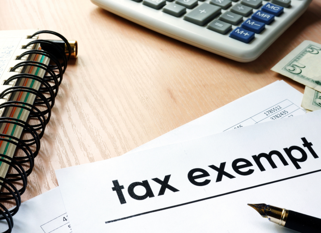 Close-up of documents labeled “tax exempt” on a desk with a calculator, cash, and office supplies.