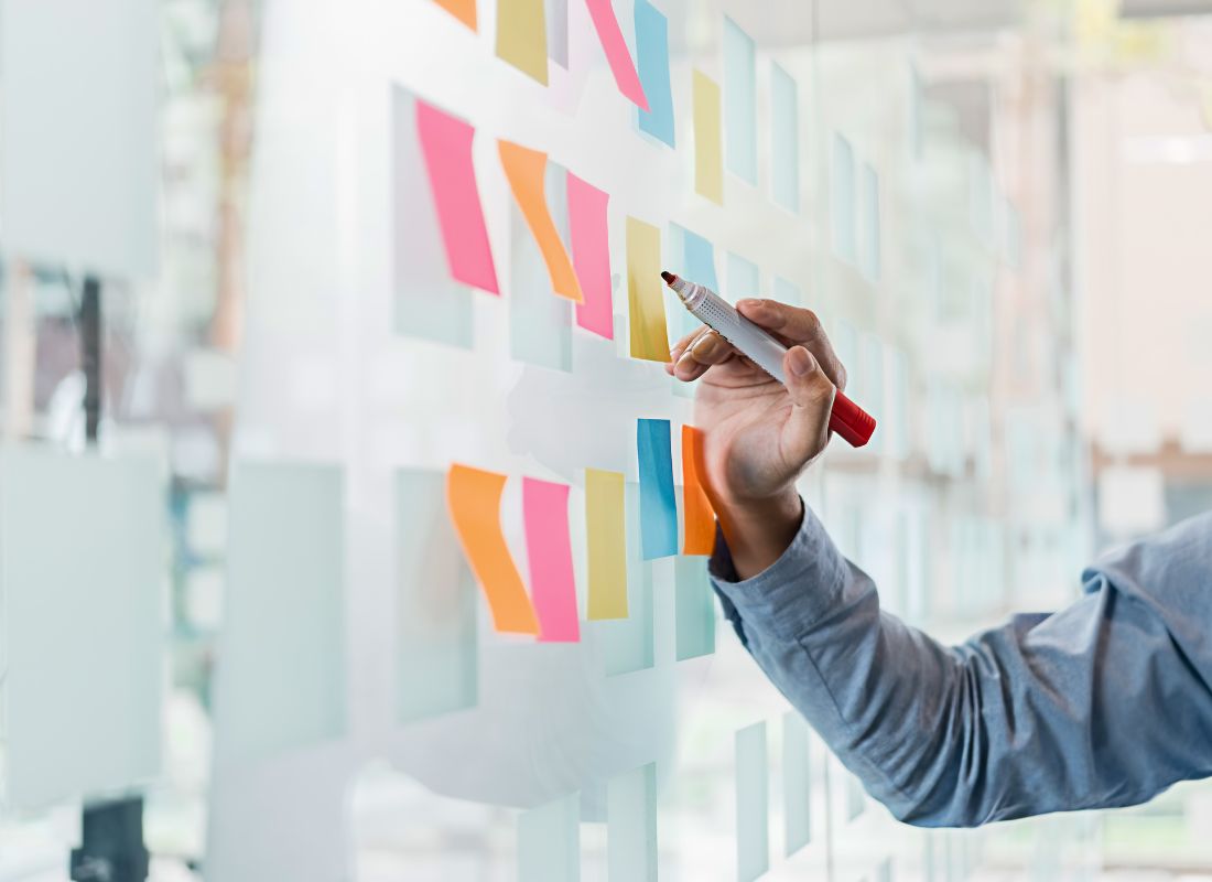 A nonprofit team member arranges colorful sticky notes on a glass wall during a strategic planning session, using a marker to organize ideas, priorities, and program initiatives.