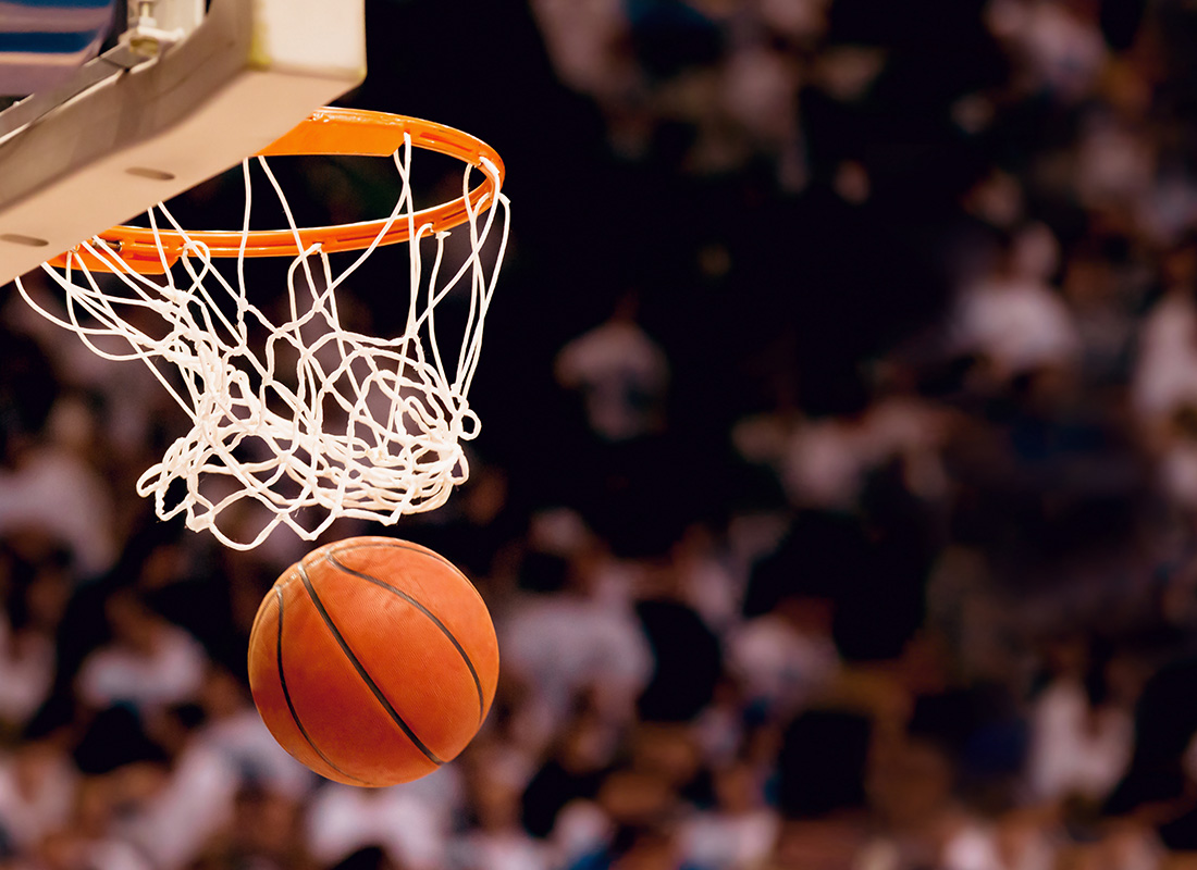 Basketball dropping through the hoop and net during a game, with a blurred crowd in the background.