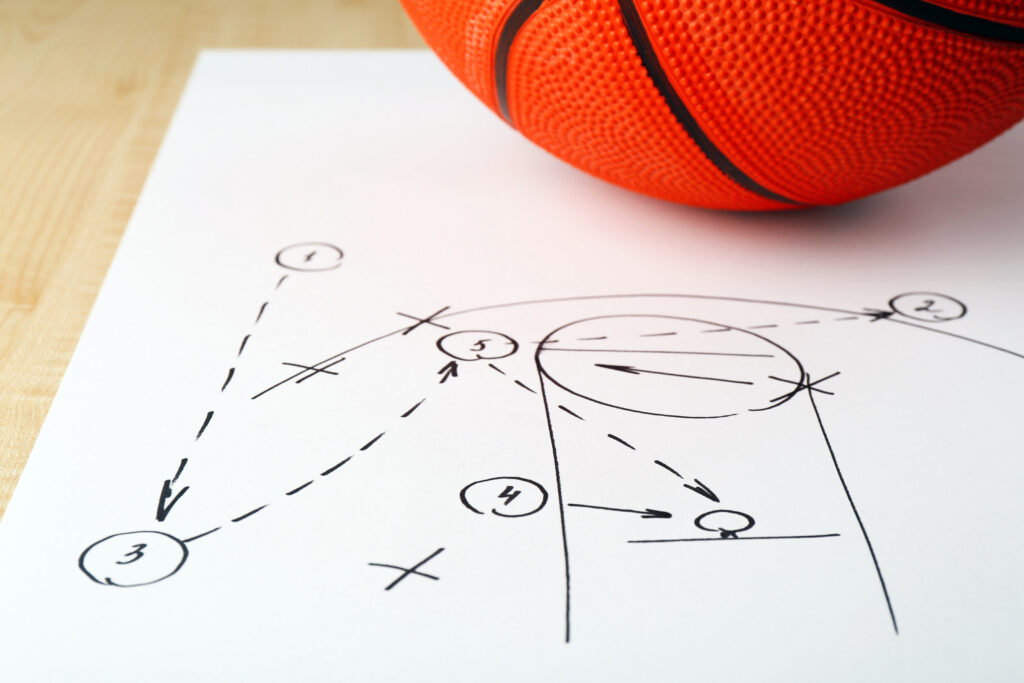 Basketball resting on a hand-drawn basketball play diagram with arrows and numbered player positions.