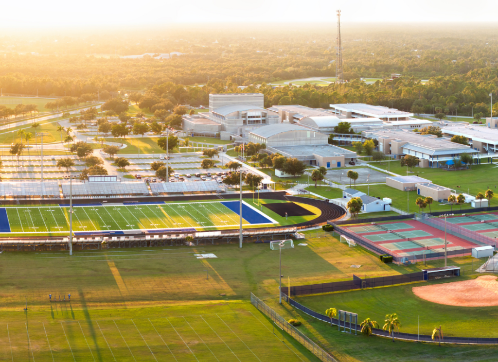 Aerial view of a college athletics complex with football and soccer fields, a running track, tennis courts, and campus facilities.