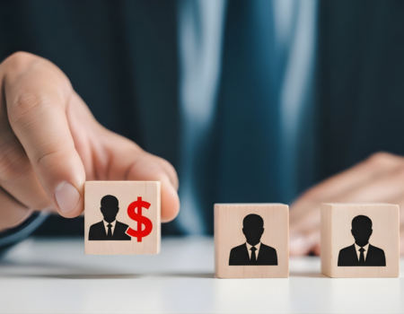 A person arranges three wooden blocks featuring businessperson icons, with one block marked by a red dollar sign.