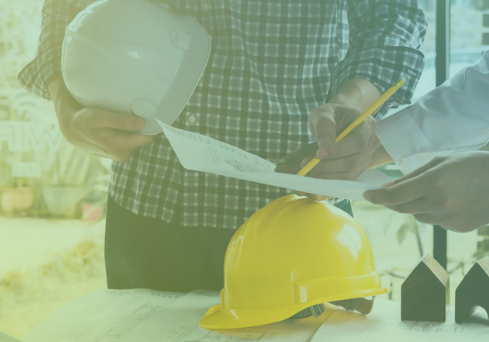 Builder's risk insurance featured image Two people examine a document over a table. One of them holds a hard hat and the other holds a pencil. A hard hat and papers lay on the table.