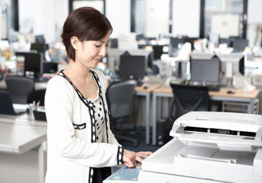 GASB 87 implementation featured img 1100 x 800 A woman is using a copy machine in an office setting. She is facing the copier while smiling and pressing a button.