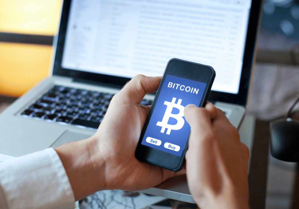 IRS new guidelines featured image A smartphone is pictured with a cryptocurrency logo displayed on the screen. A laptop computer is open in the background.
