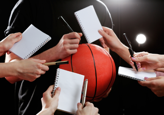 NIL wellbeing Featured image An athlete signs a basketball while fans hold out pens and pads of paper, waiting for their turn to get an autograph.