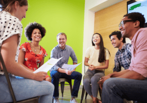 NP CPE Series blog post featured image 1100 x 800 (19) A group of six people are sitting on chairs in a circle and smiling.