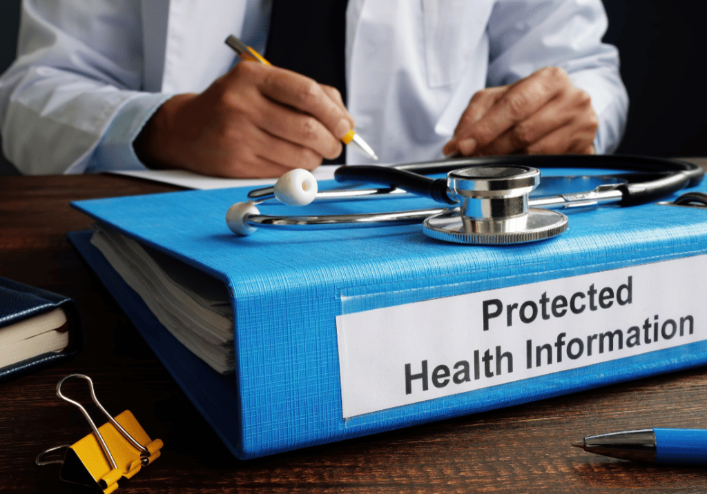 A Doctor in a white coat is sitting at a desk, writing with a pen. A Stethoscope sits on top of a large binder labeled "Protected Health Information."