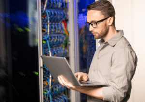 Preparing for Disaster featured image (31) An IT professional is standing in a server room evaluating the IT servers with his laptop.