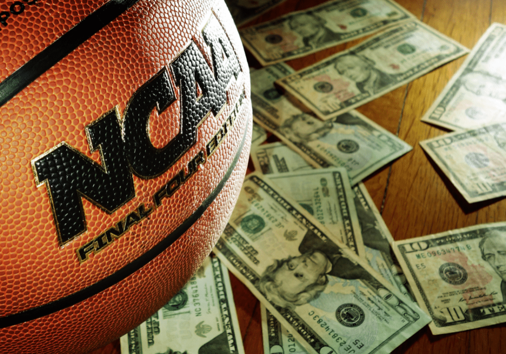 An NCAA basketball is shown on a hardwood floor surrounded by cash.