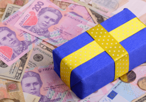 A gift wrapped in blue and yellow wrapping paper is sitting on top of money. The money is mostly U.S. and foreign cash, with a few foreign coins.