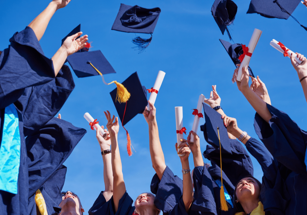 featured image 1100 x 800 - 2023-05-17T115924.815 A group of new graduates wearing graduation gowns, are holding up their diplomas and throwing their graduation caps in the air.
