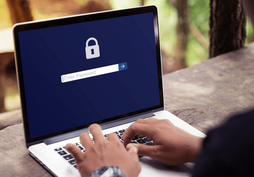 featured image 1100 x 800 - 2023-05-17T124848.121 An laptop is sitting open on a desk with a lock on the screen and a text box that says, "Enter Password". A person's hands are shown typing on the computer and the background is blurred.