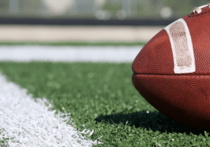 The nose of a football is shown on a football field next to a yard line.