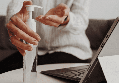 closeup of employee using hand sanitizer by computer in compliance with COVID-19 workplace guidance